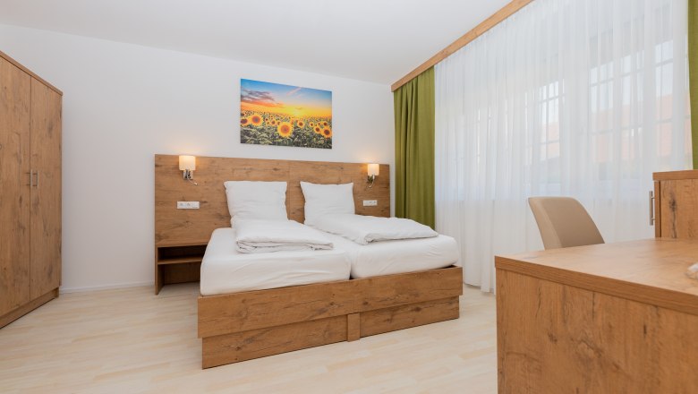 Modernes Schlafzimmer mit Holzmöbeln, Doppelbett, Schrank und Schreibtisch. Ein Bild mit Sonnenblumen hängt über dem Bett.