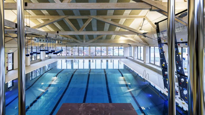 Interior view of a modern indoor pool with swimming lanes and climbing wall.