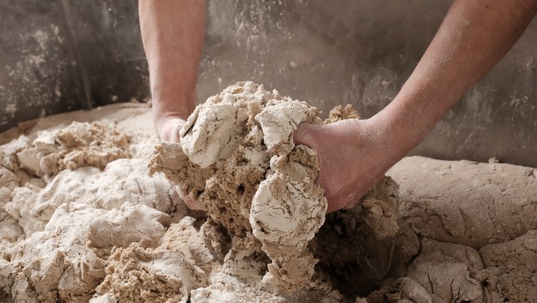 Hands knead dough in a large bowl.