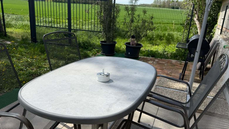 Gartentisch mit Stühlen auf einer Terrasse, umgeben von grünem Rasen und einem Zaun.