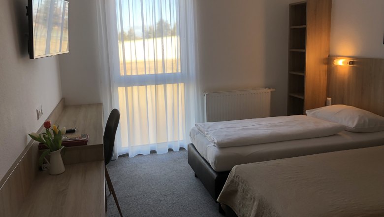 A simply furnished motel room with two single beds, a desk, a TV and a window with curtains.