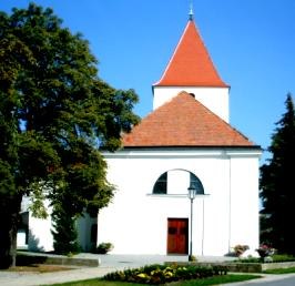 White church with red roof and tower, surrounded by trees.