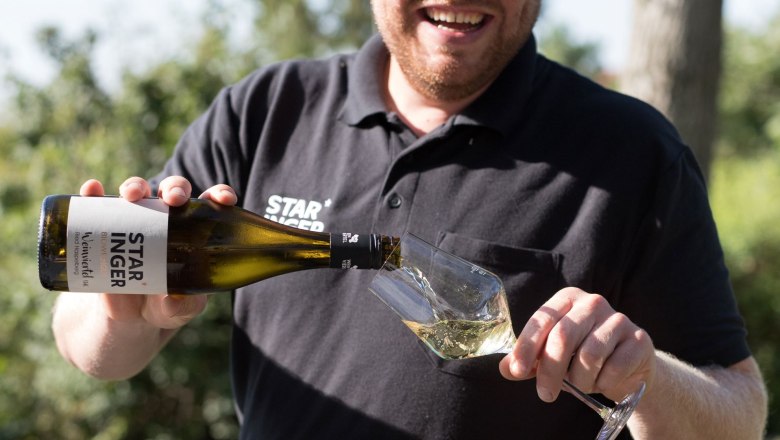 Mann schenkt Wein in ein Glas im Freien ein.