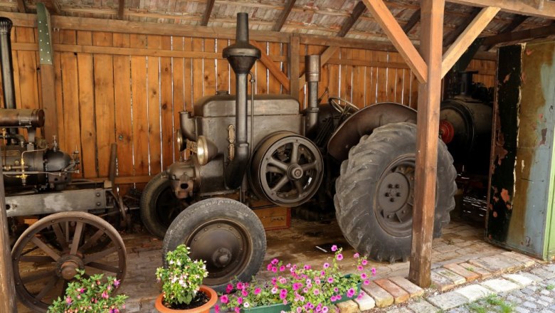 Old steam engines in a wooden shed with flowers in the foreground.
