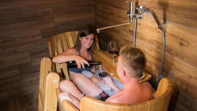 Two people in a wooden tub shower with wine.