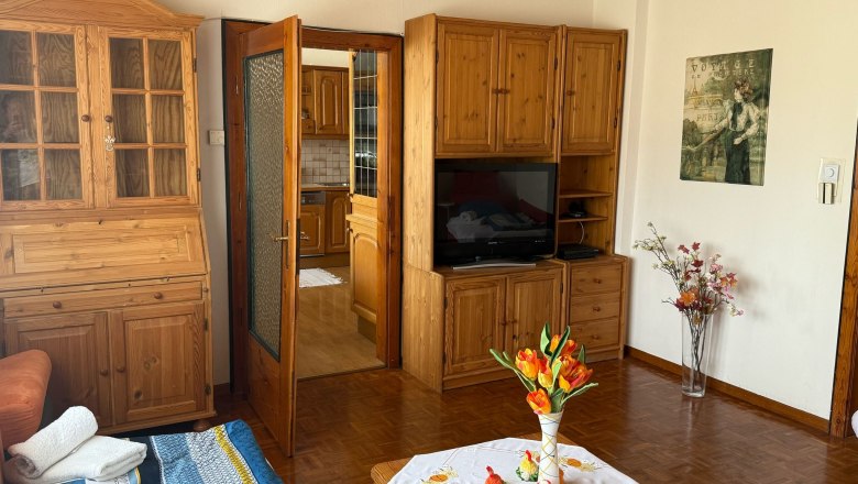 Wohnzimmer mit Holzmöbeln, einem Tisch mit Blumen und einem Fernseher.